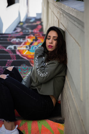 Women's olive crop top hoodie sitting on a staircase in downtown Los Angeles